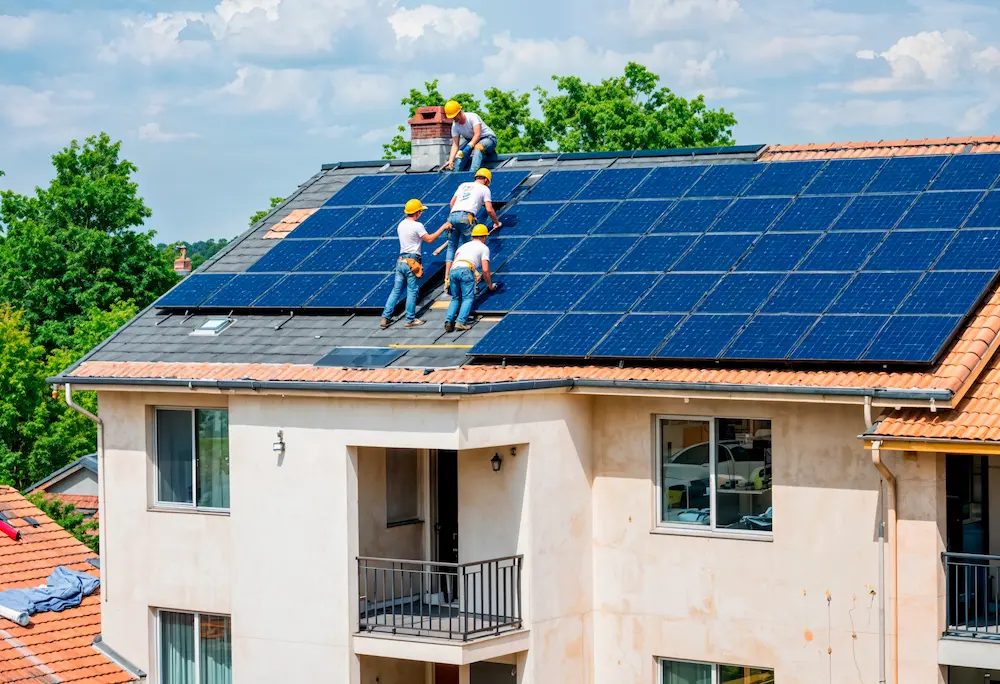 Technicians cleaning and maintaining rooftop solar panels on residential building in Kerala